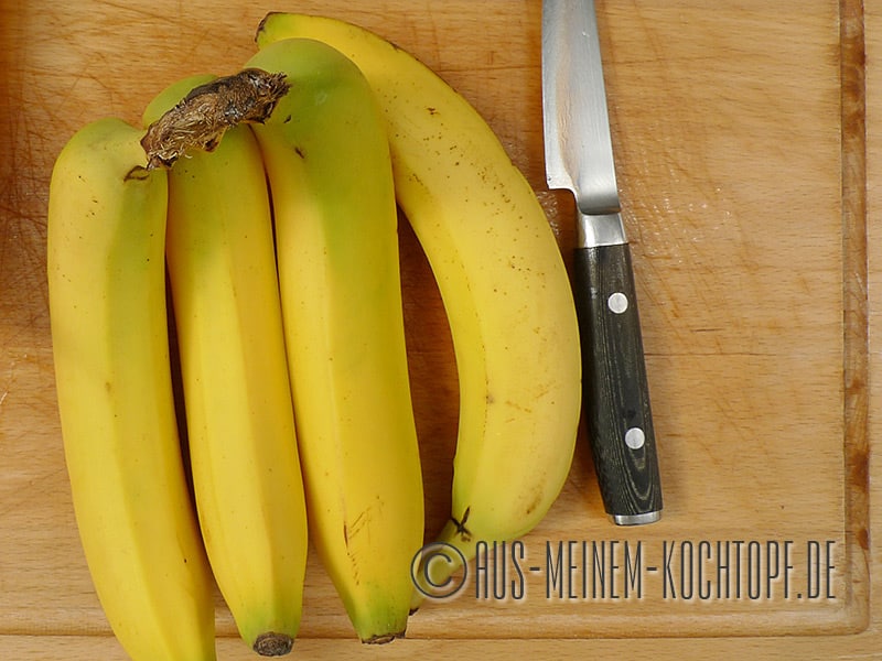 Die Bananen seitlich hinlegen und von jeder Frucht zuerst unten ein kleines Stück der Schale abschneiden